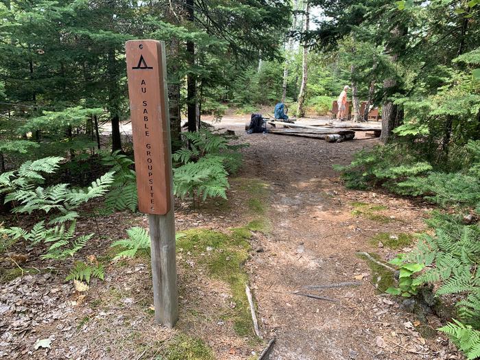 Sign reads Au Sable Group Site. Dirt path leads to campsite in the background.