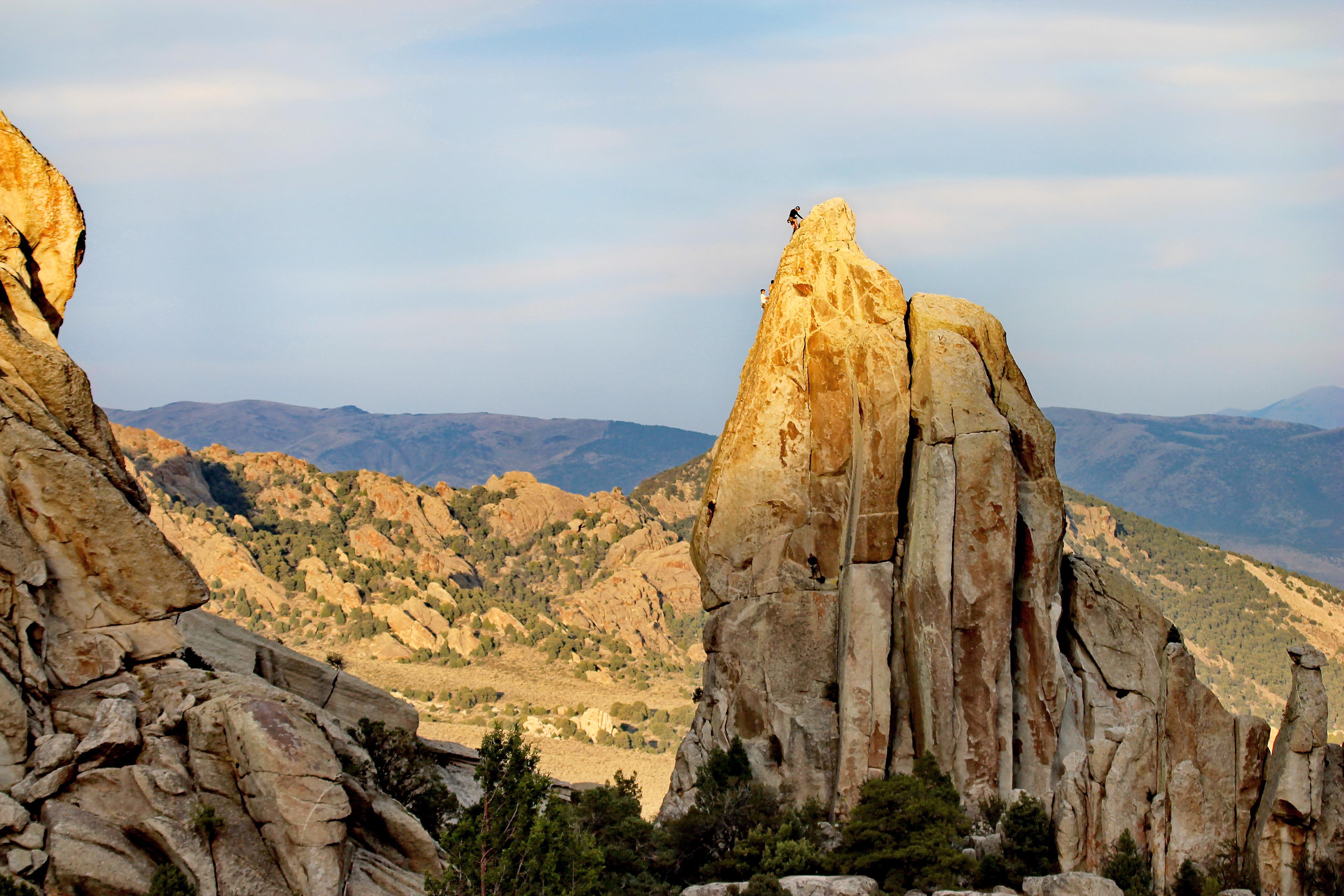 A climber ascends a granite spire with mountains in the distance.