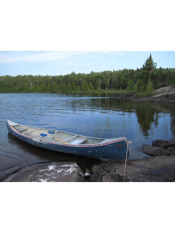 A canoe on the rocky shoreline of Wood Lake stretching into the water with scenery.