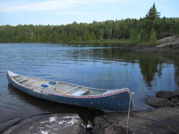 A canoe on the rocky shoreline of Wood Lake stretching into the water with scenery.