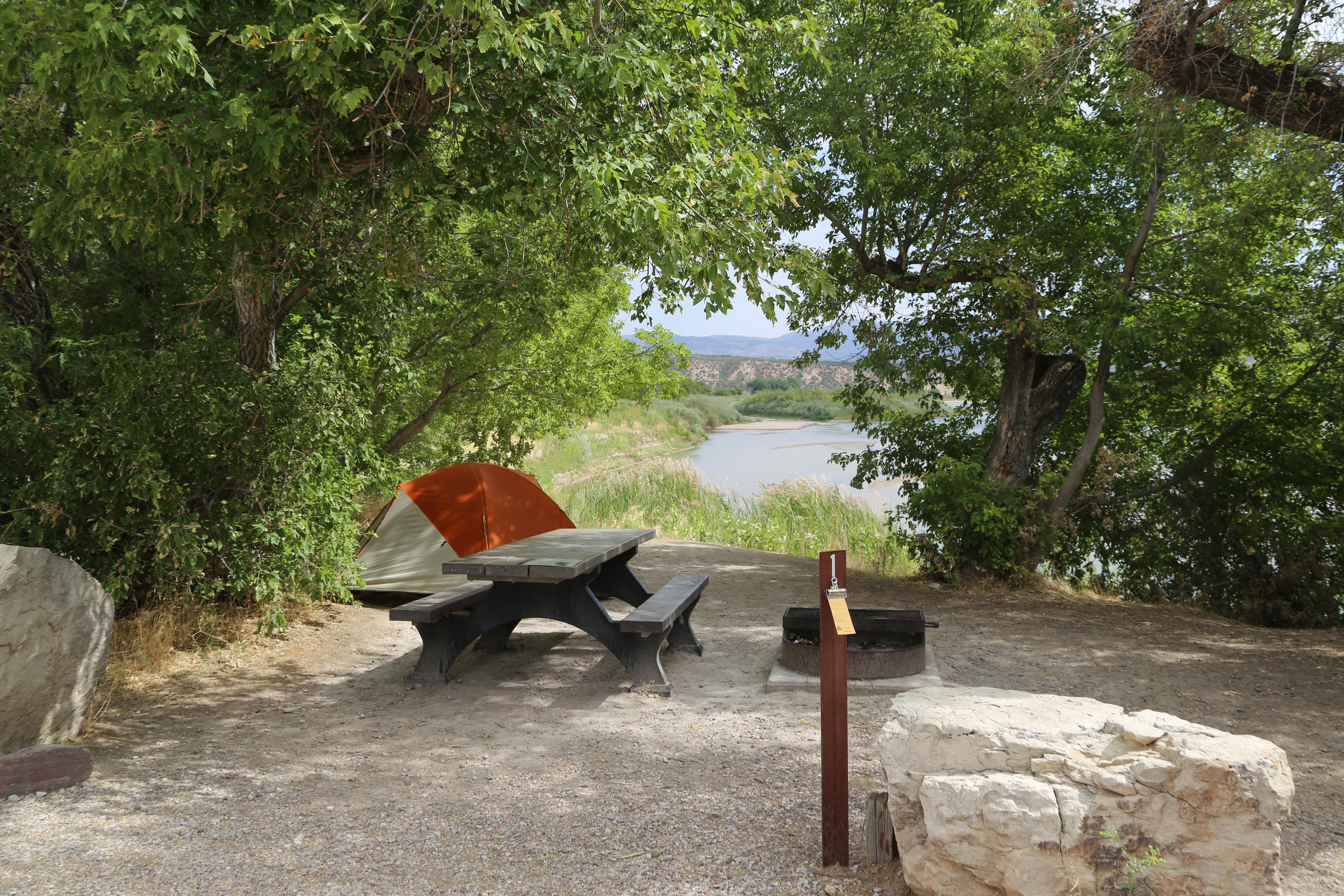 Picnic table and tent at a campsite with a river in the background.