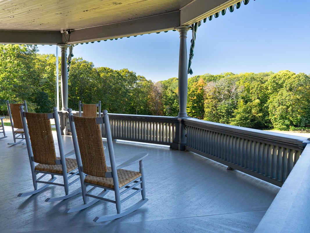 Two rocking chairs on a large porch with a view of a field and trees.