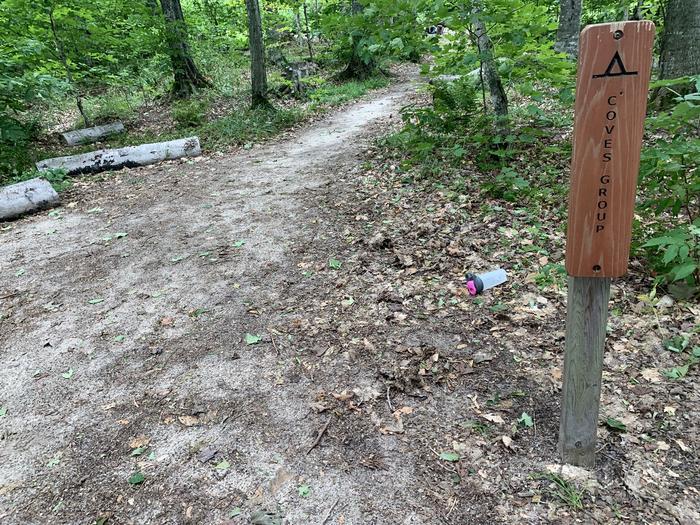 Sign reads Coves Group with a dirt trail leading through forest.