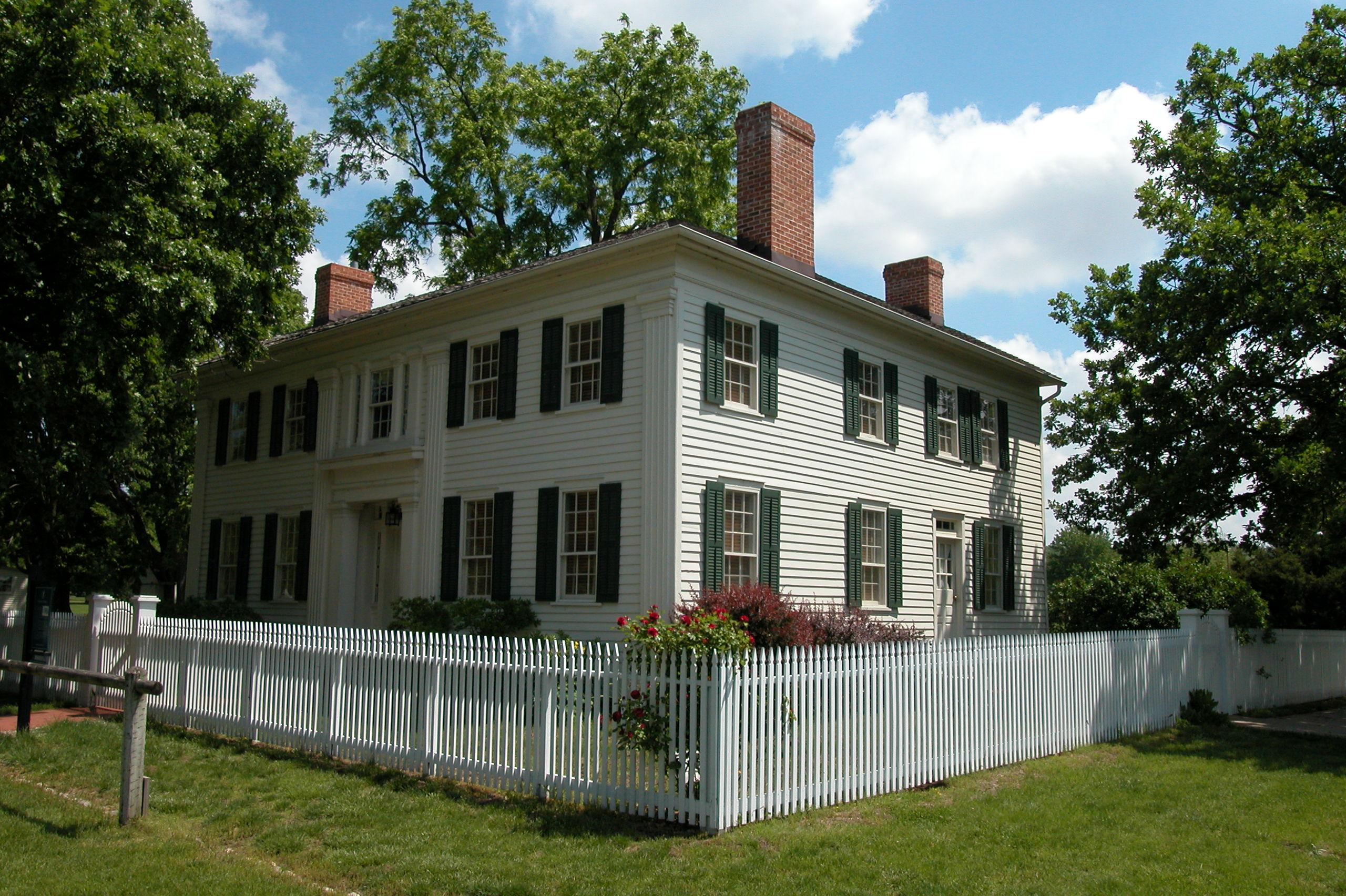 A large, white, two-story historic wood home with a red roof and white picket fence.