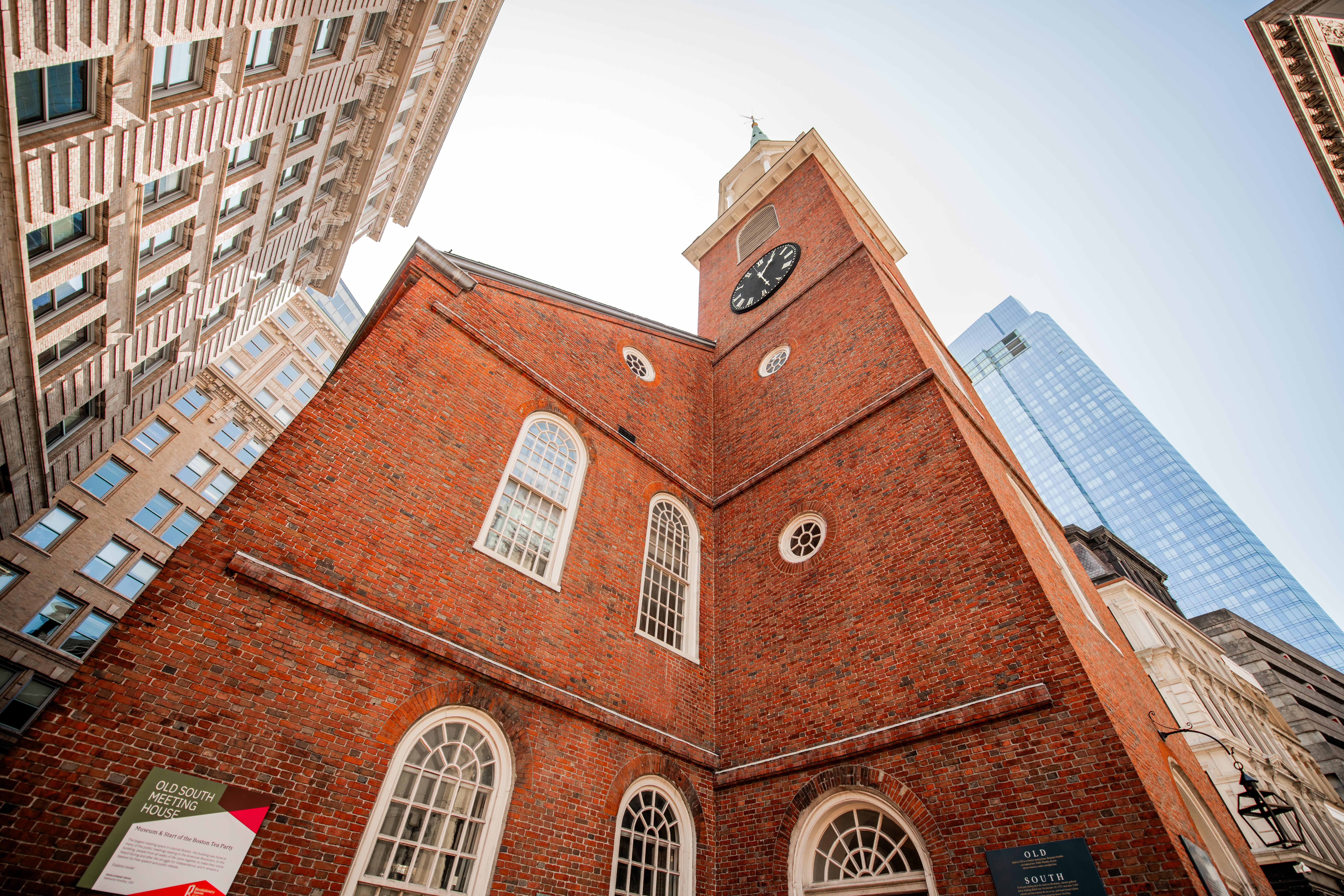 Looking up at a brick meeting house with a tall white steeple.