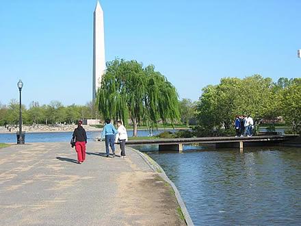 People walking on a sidewalk near water and a bridge