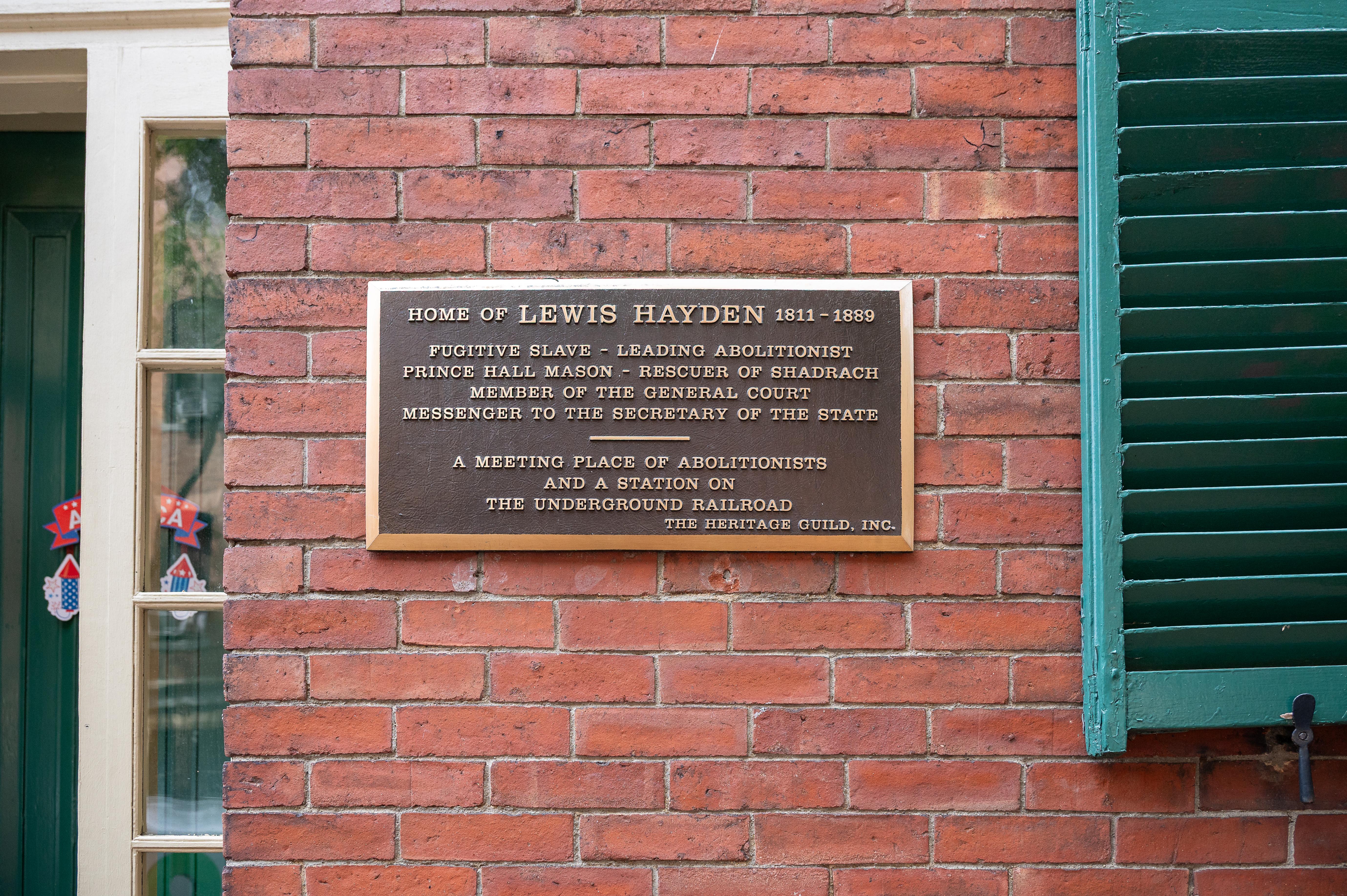 Close up of a plaque on the brick facade of the Hayden House, which has green shutters