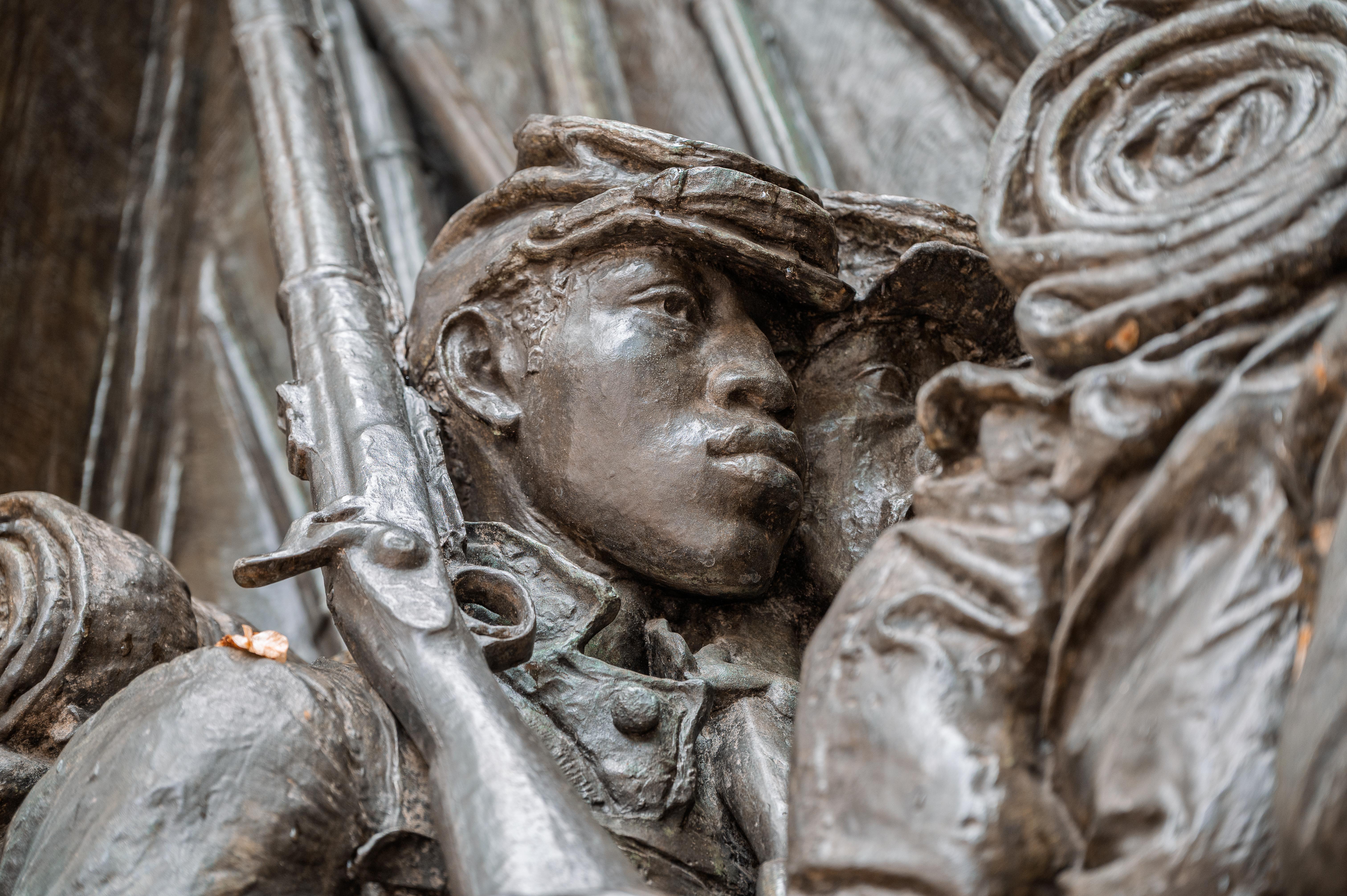 Close up of a bronze relief of a young soldier carrying a rifle.