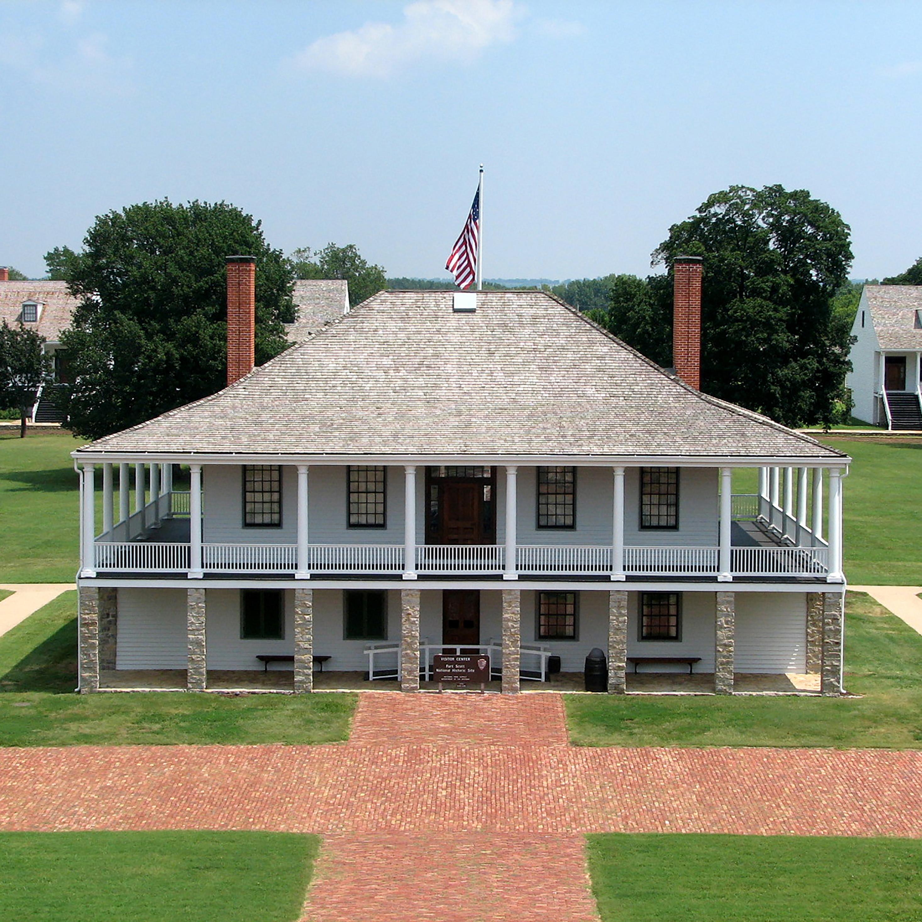 Picture of the post hospital with the parade ground and trees in the background.