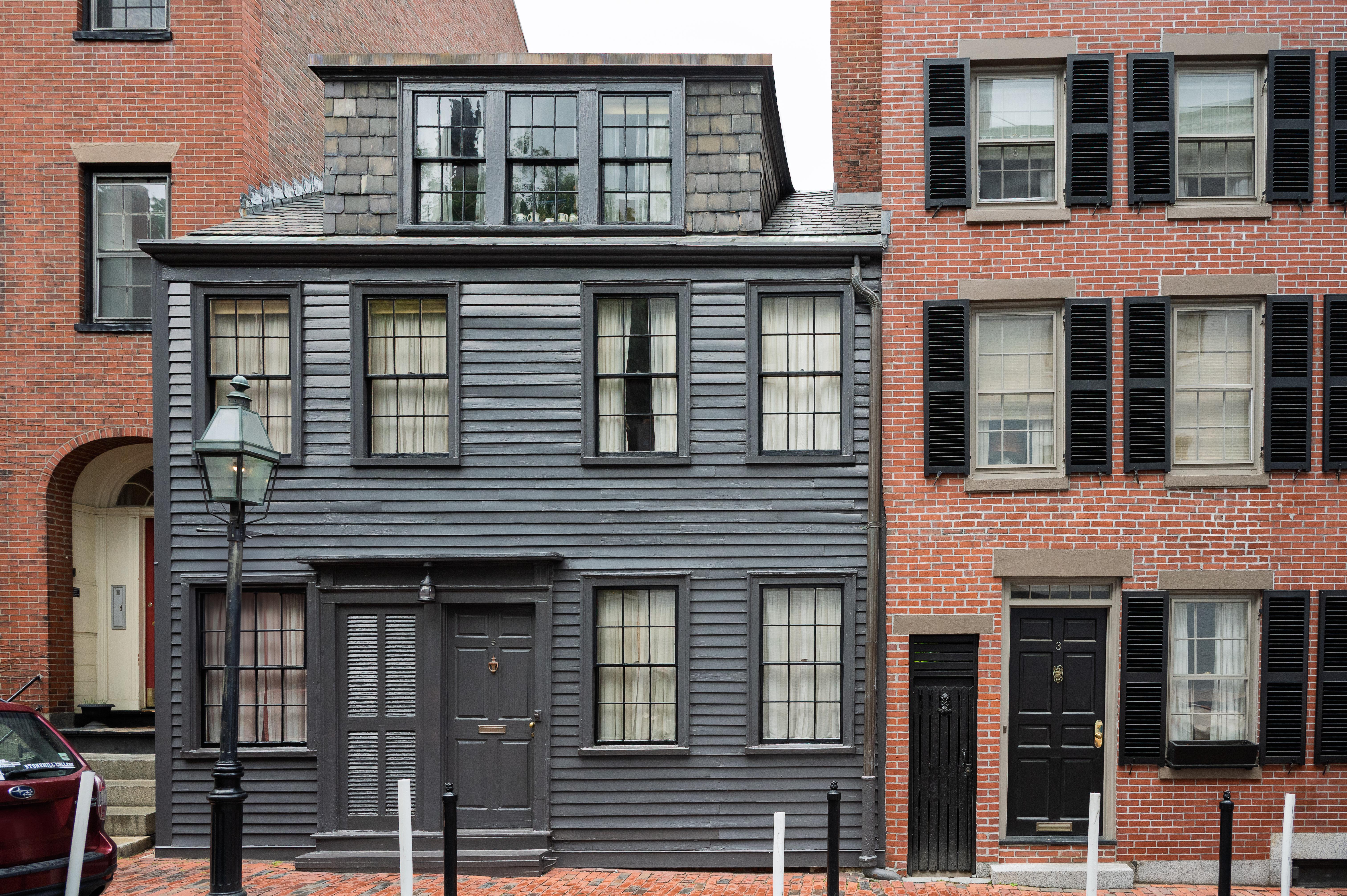 Small gray wood building in between two brick buildings