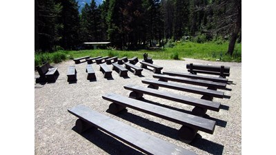 wooden benches on gravel clearing with campsites and bathroom building in background among trees