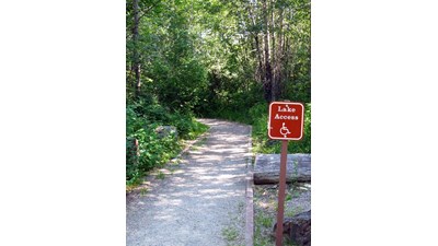 hard packed trail in woods marked with accessible symbol on sign