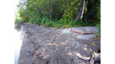 hardpacked gravel pad at forest edge, dark sandy beach at shoreline