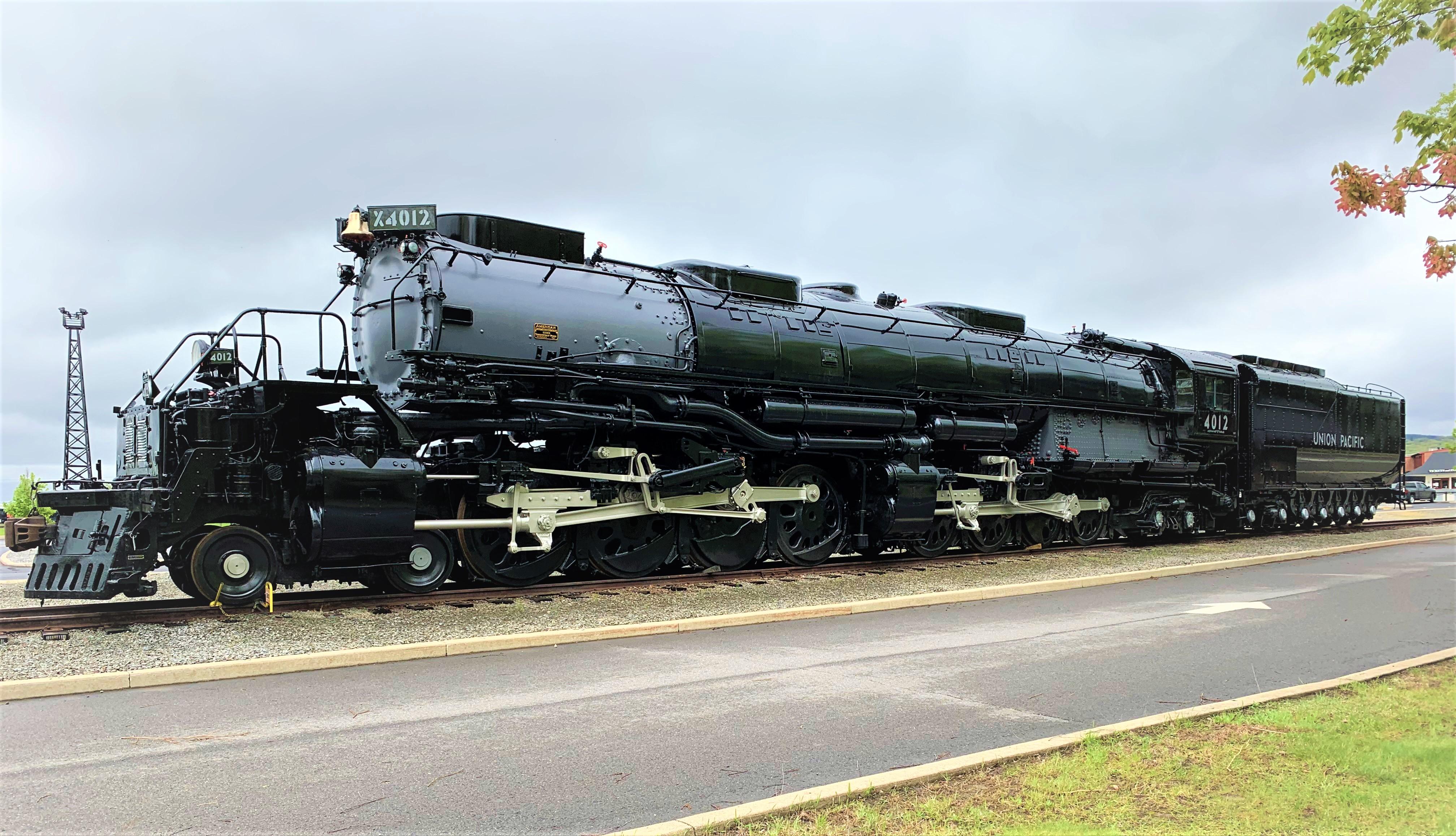 large black train stationed on a track to the left of a paved road