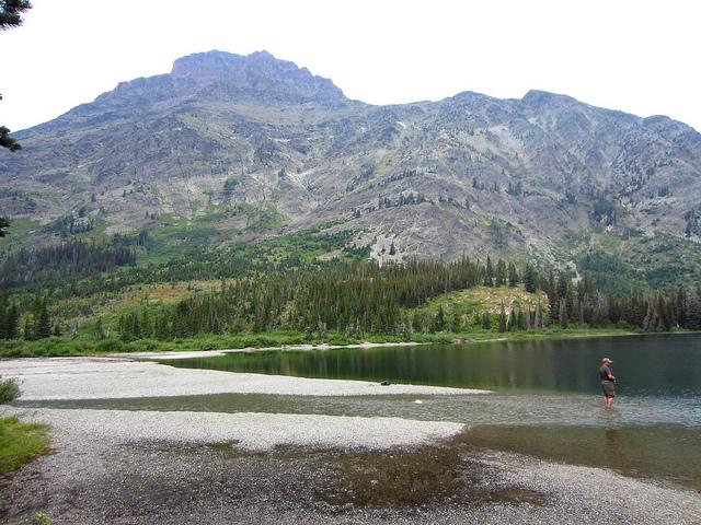 man stands in shallow water of small lake at base of mountain