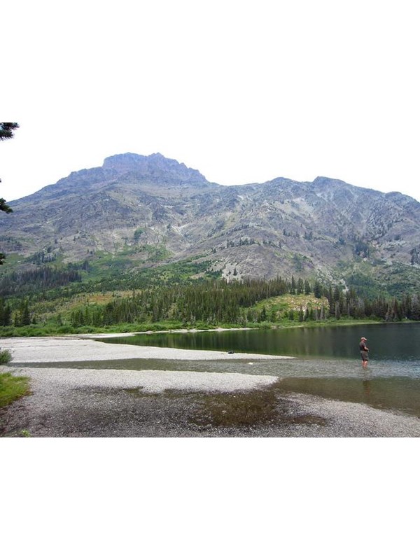 man stands in shallow water of small lake at base of mountain