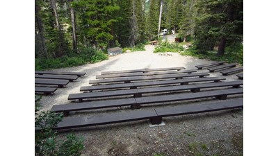 long wooden benches in gravel clearing with picnic table and food storage box in background