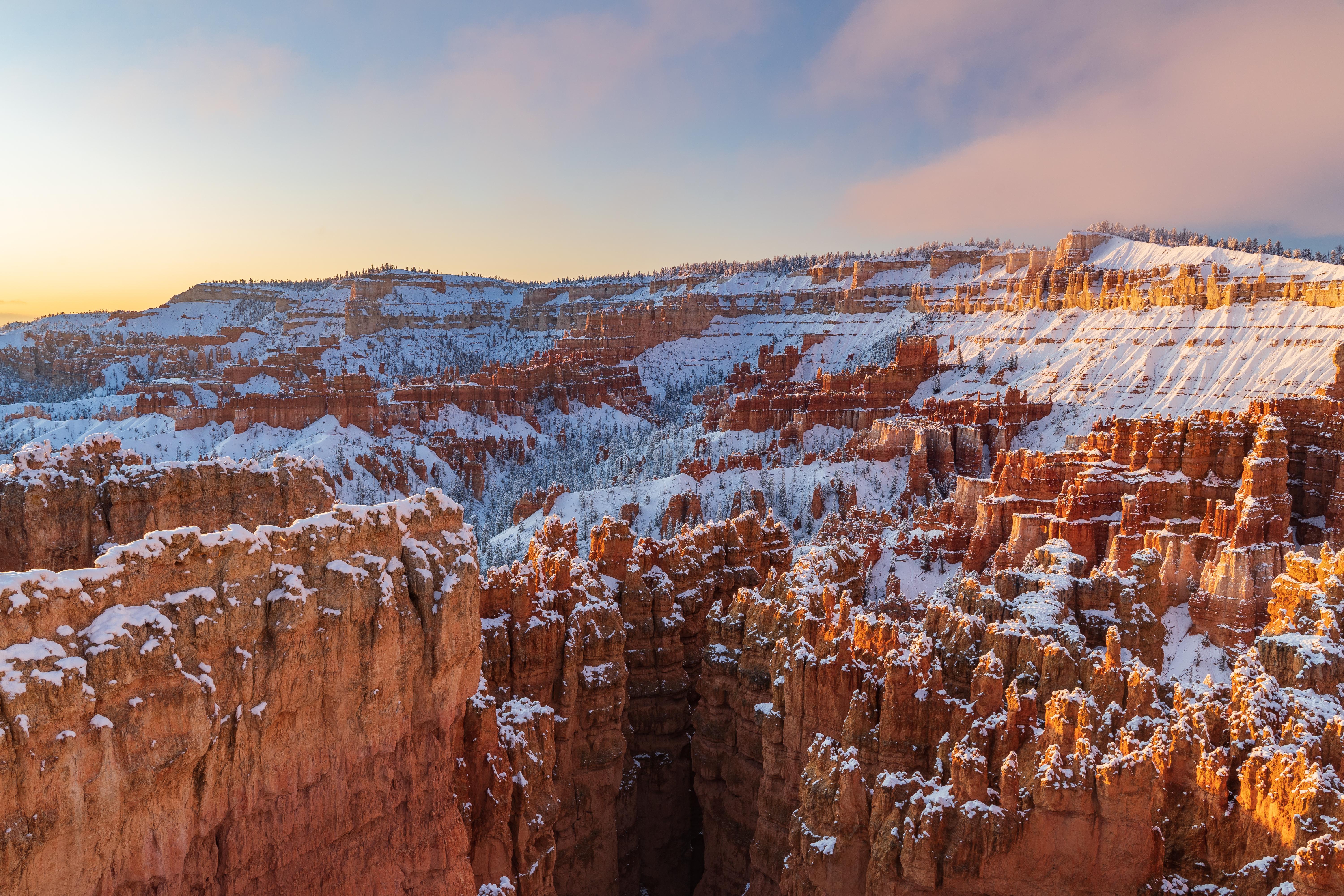 Snow blankets a red rock landscape of tall rock spires beneath an early morning sky
