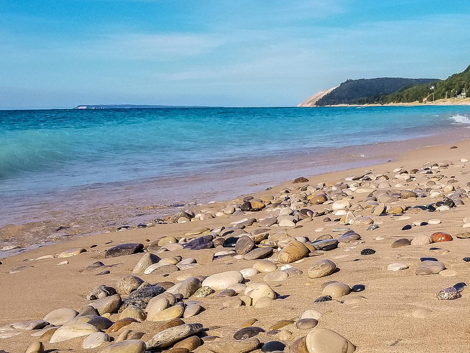 Sand and pebbles in foreground with turquoise water in background