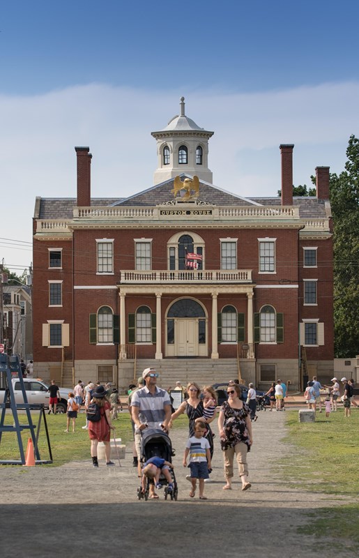 A group of people walk in front of a large brick Custom House