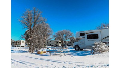 Several RVs parked in individual sites with several inches of snow covering the ground.