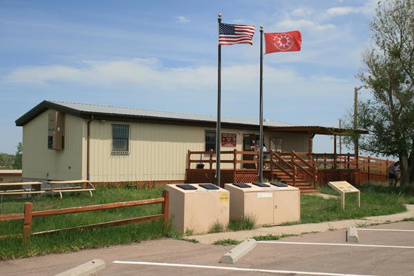 Double-wide trailer under blue sky with USA and Oglala Sioux Tribe flags.