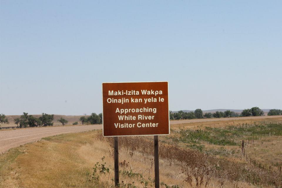 Tan sign with Lakota and English phrases indicating that approach to White River Visitor Center.