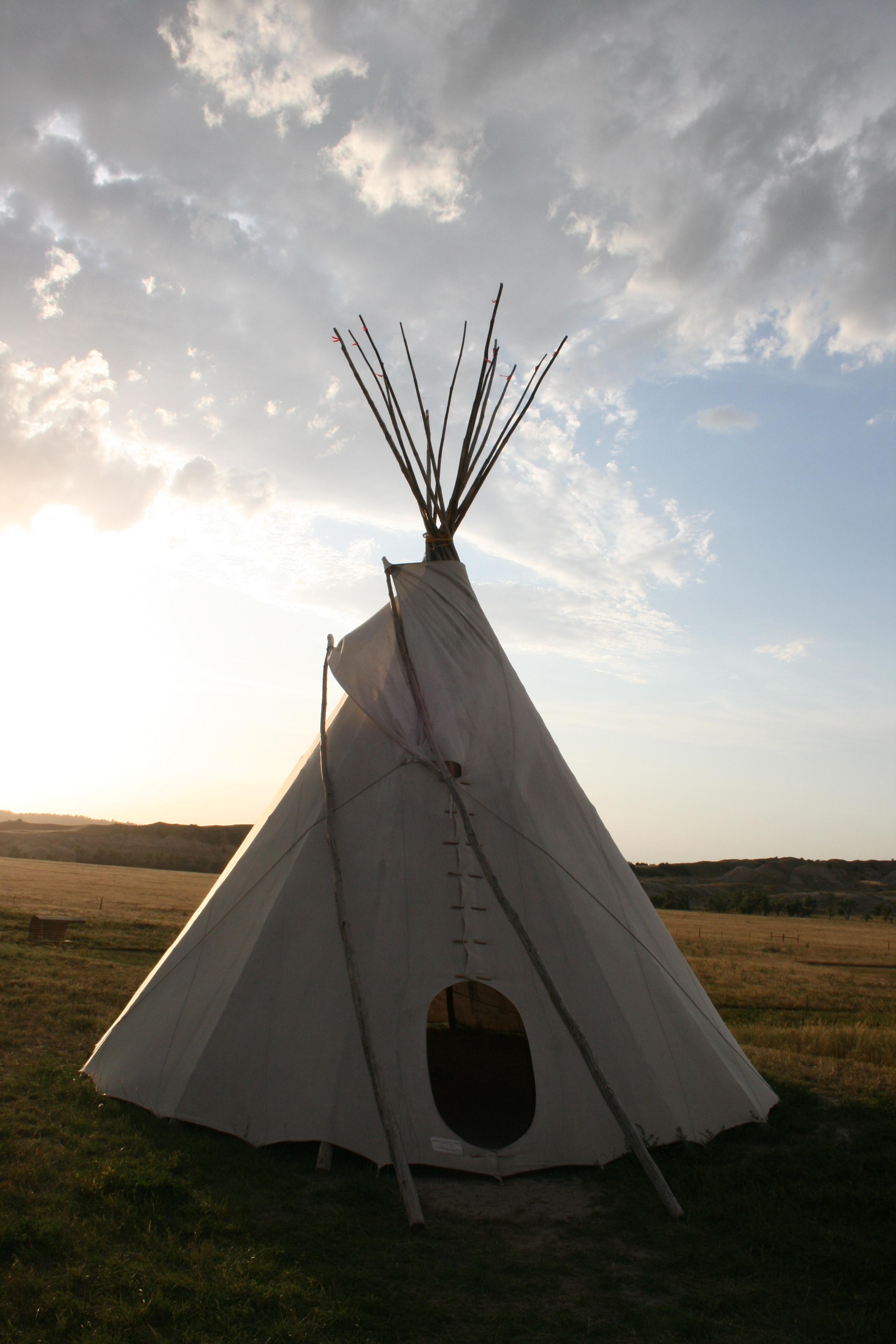 White canvased Tipi under partially cloudy sky amid prairie grasses.