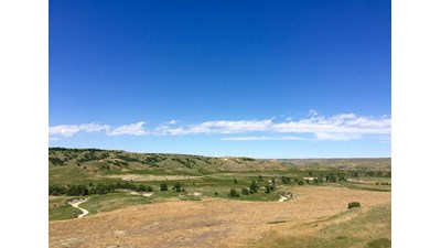 Dirt road meanders around several camping sites amid prairie grass and under blue sky.
