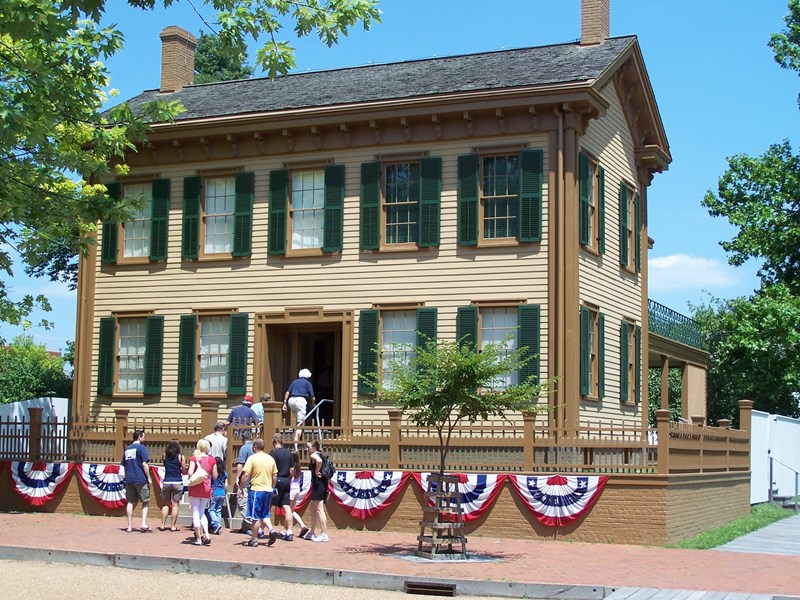A guide leading a group into the Lincoln Home which has bunting on the front.