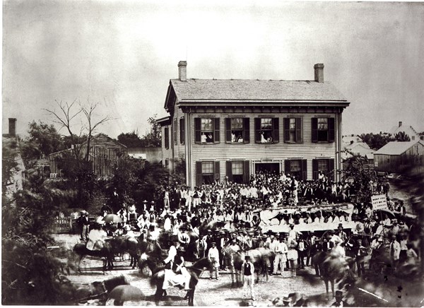 A black and white image of a crowd of people standing in front of and around the Lincoln Home.