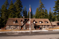 A native stone two-story building with a flagpole out front and tall conifers behind