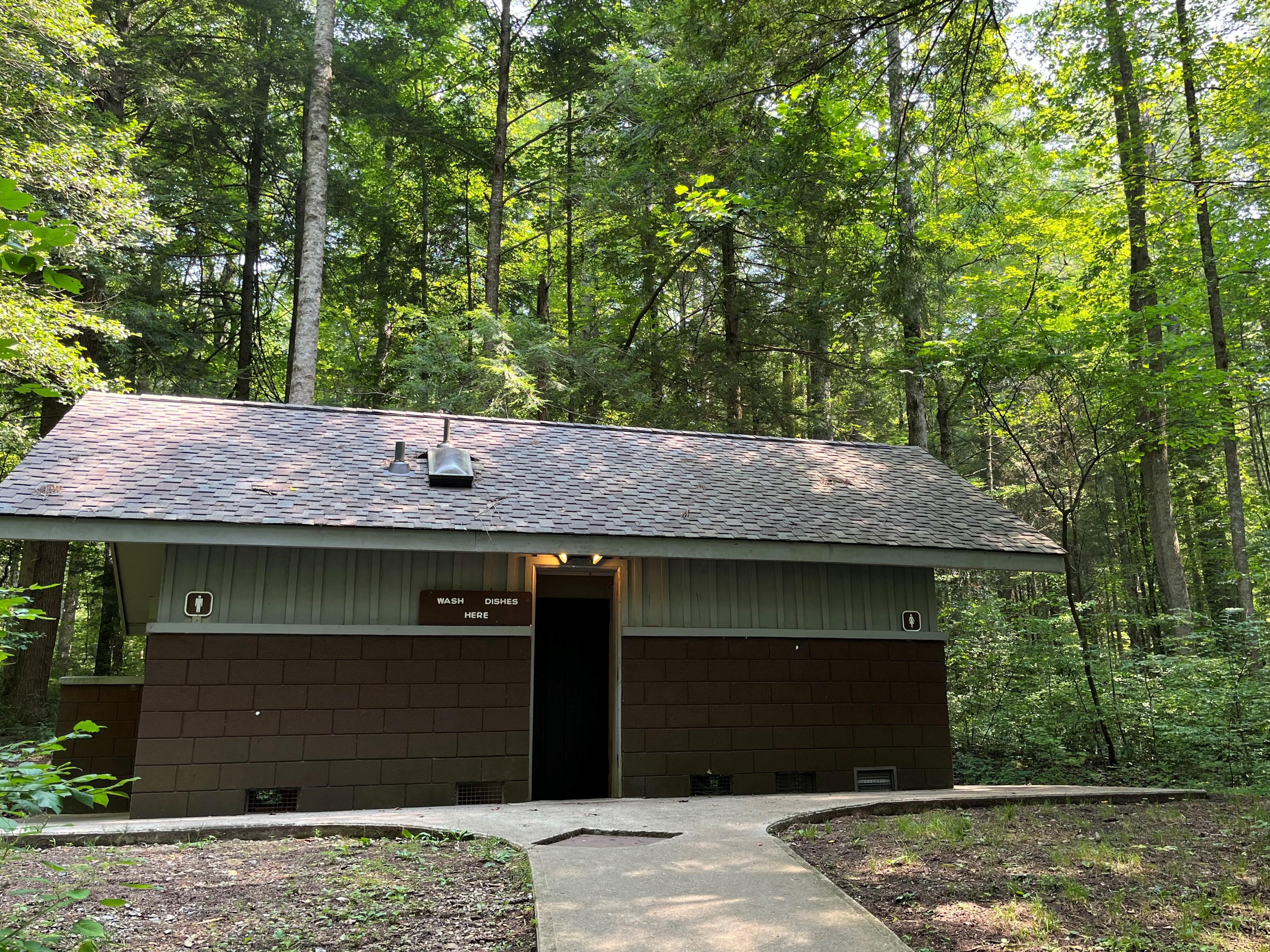 A campground restroom with a paved pathway to it. A sign beside a door says, "Wash dishes here".