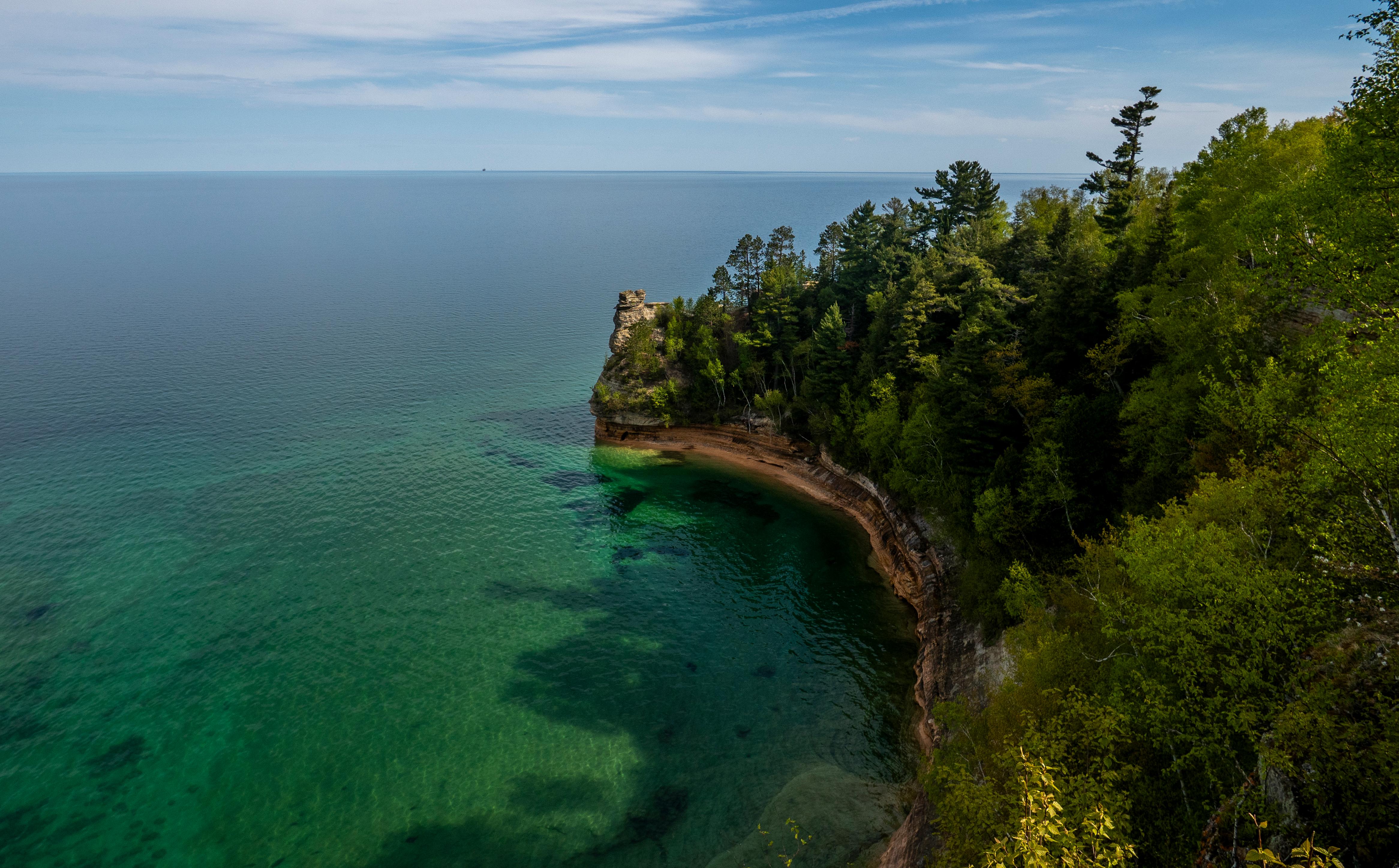 A sandstone rock formation rises out of a blue-green Lake Superior on a sunny day.