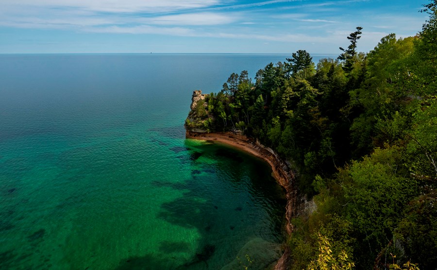 A sandstone rock formation rises out of a blue-green Lake Superior on a sunny day.