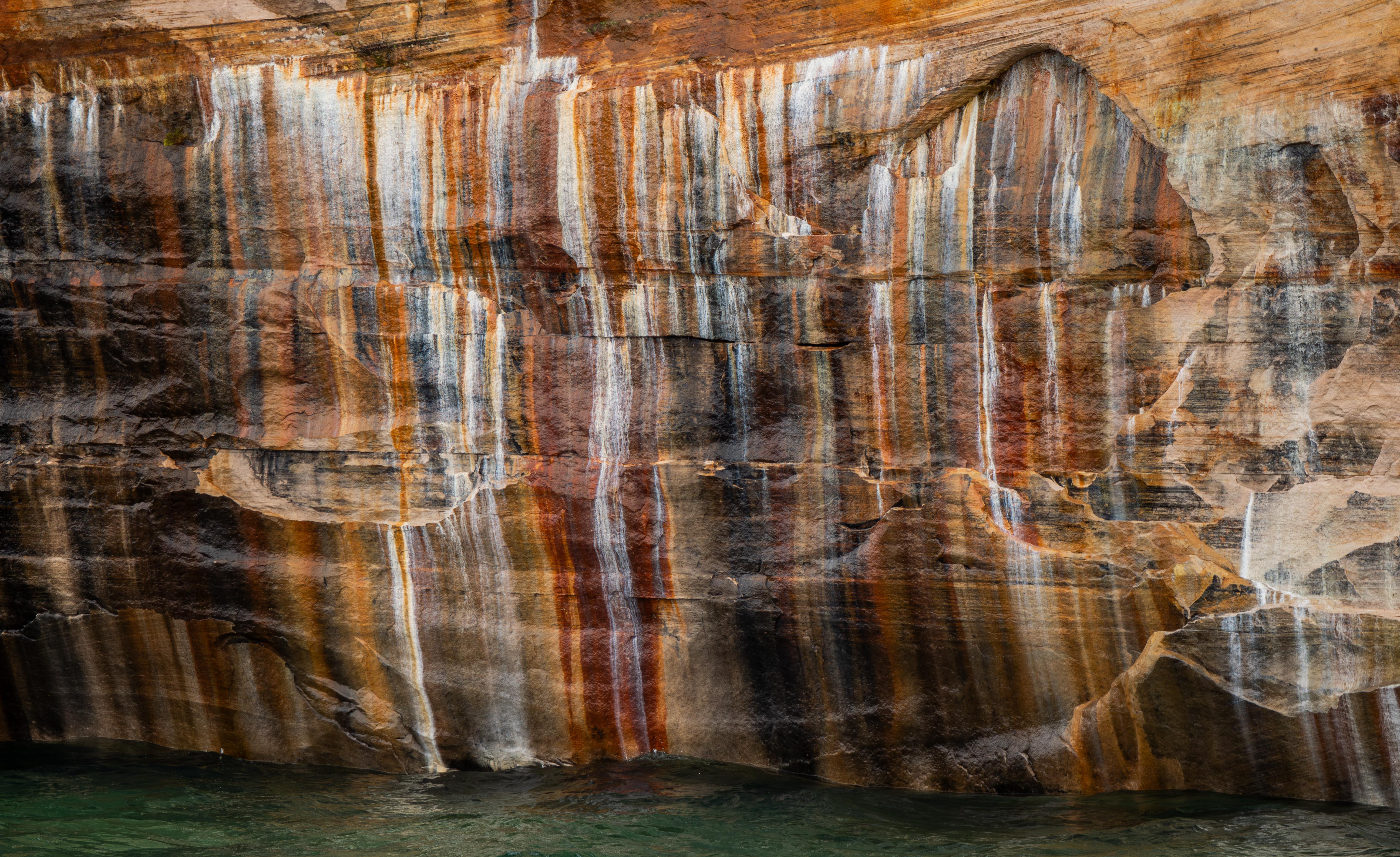 Orange, black, and white mineral streaks cover a sandstone cliff face.