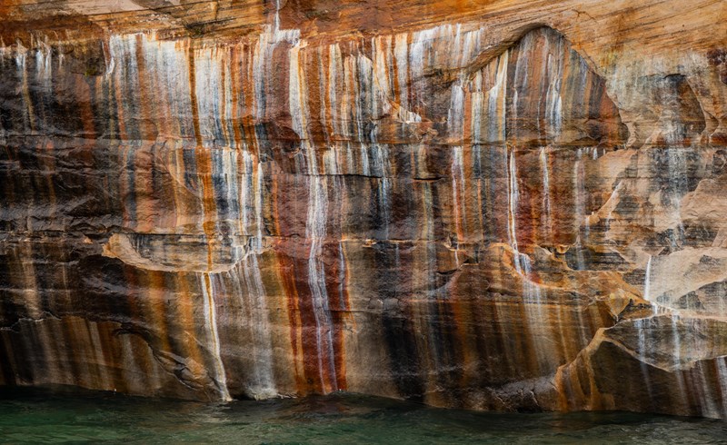 Orange, black, and white mineral streaks cover a sandstone cliff face.
