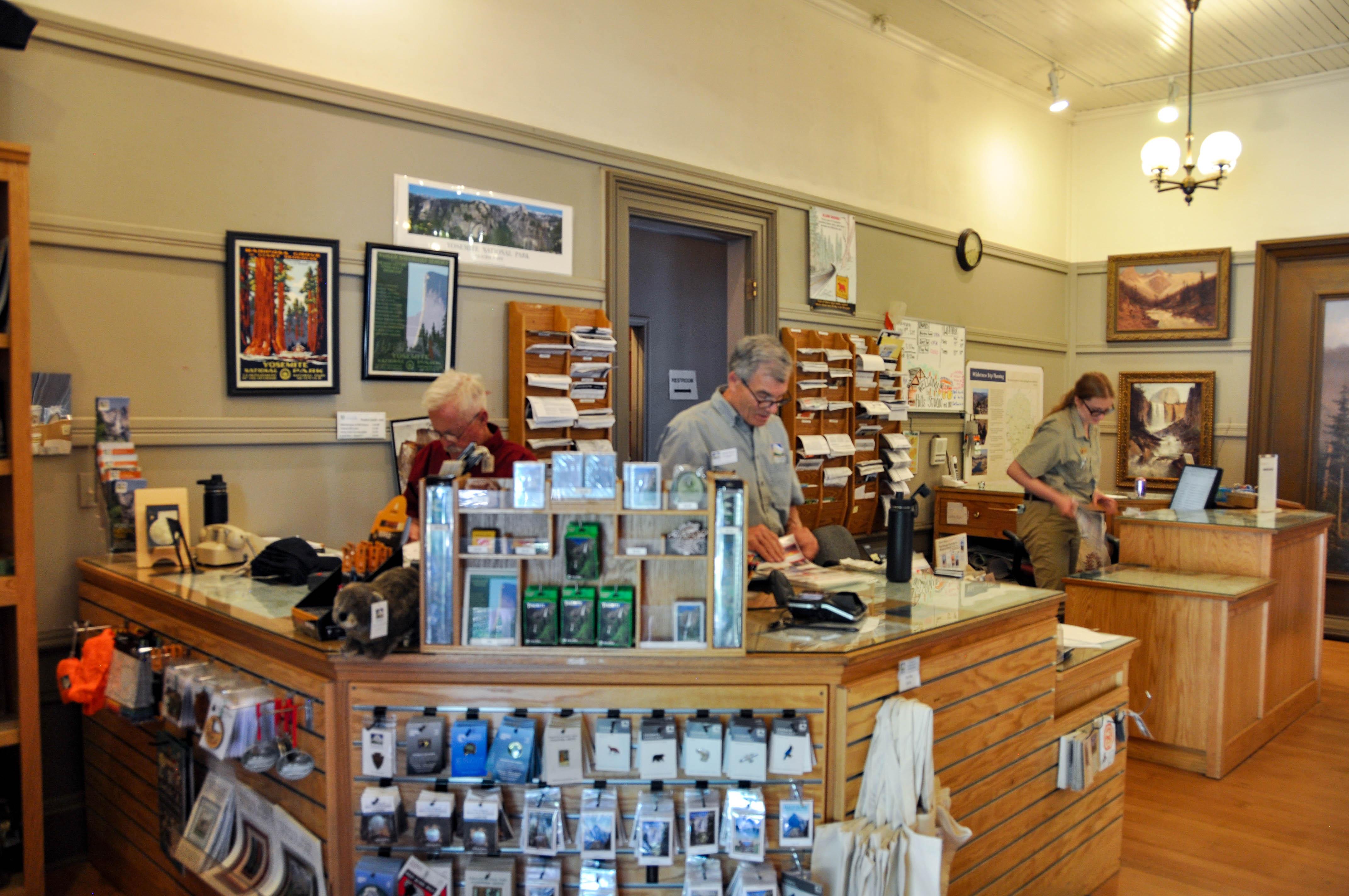Three people stand behind an information desk that is surrounded by store merchandise.