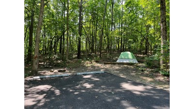 A white tent with a light green rainfly near a picnic table, fire ring, and two paved parking spots.