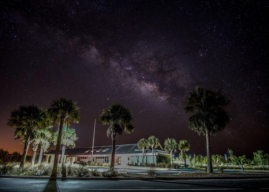 The milky way dominating a starry night sky over palm trees and a visitor center