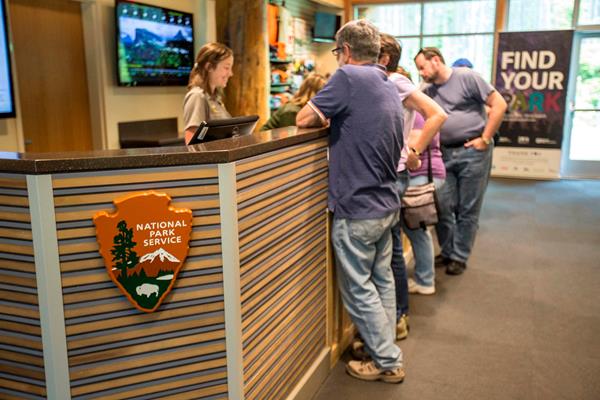 A park ranger, standing behind an information desk, assists a group of visitors.