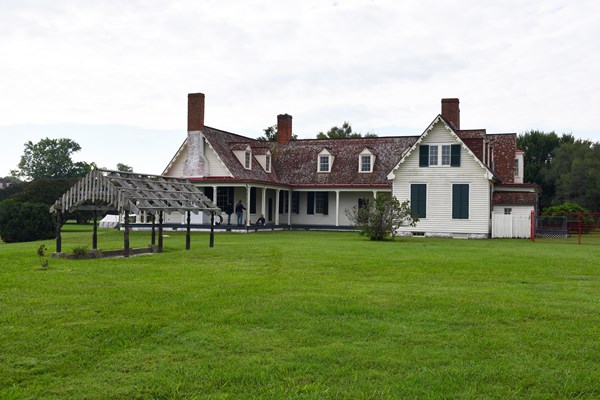 An arbor stands 20 feet in front of a two story white house with a red shingled roof.