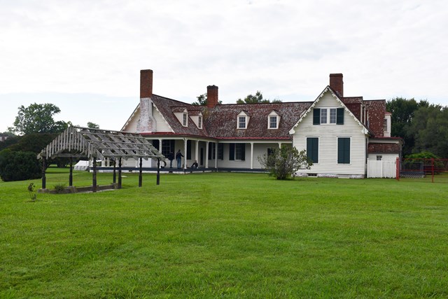 An arbor stands 20 feet in front of a two story white house with a red shingled roof.