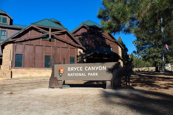 Sign reading Bryce Canyon National Park with an arrowhead stands before large brown building