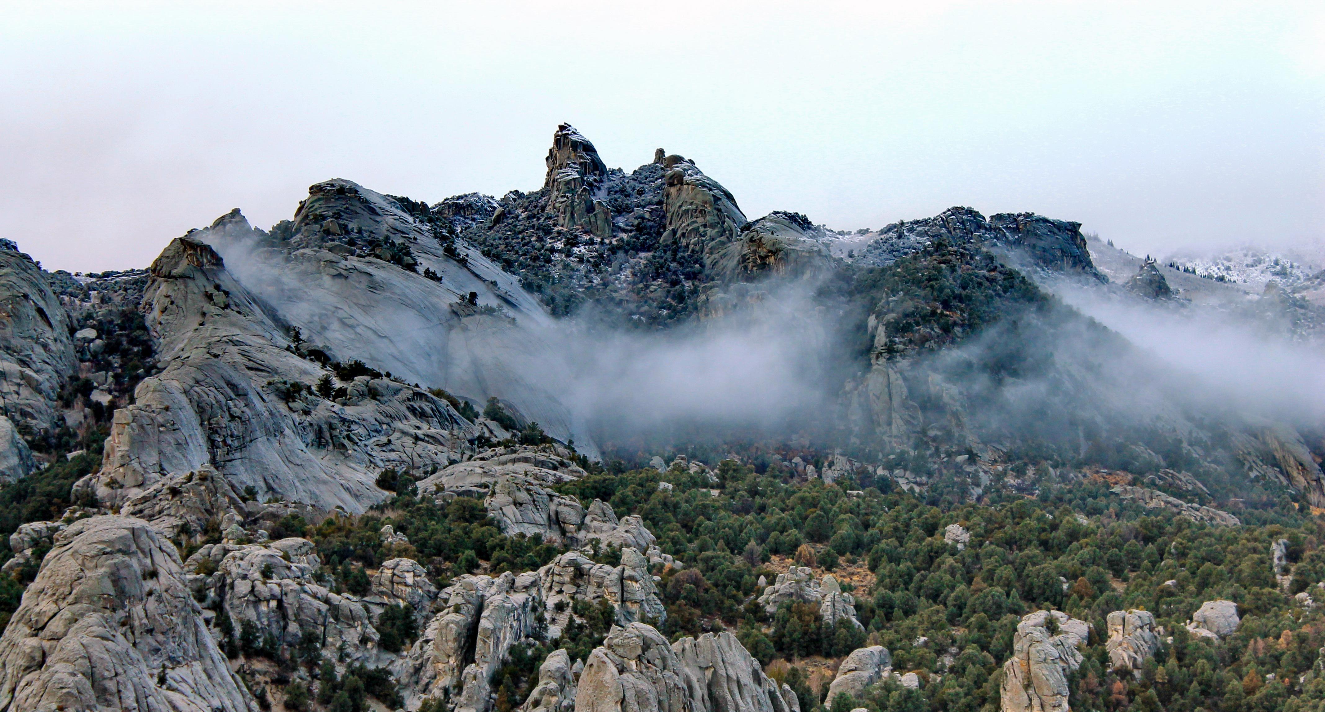 Snow dusted granite formations jut up from a mountainous juniper covered landscape.