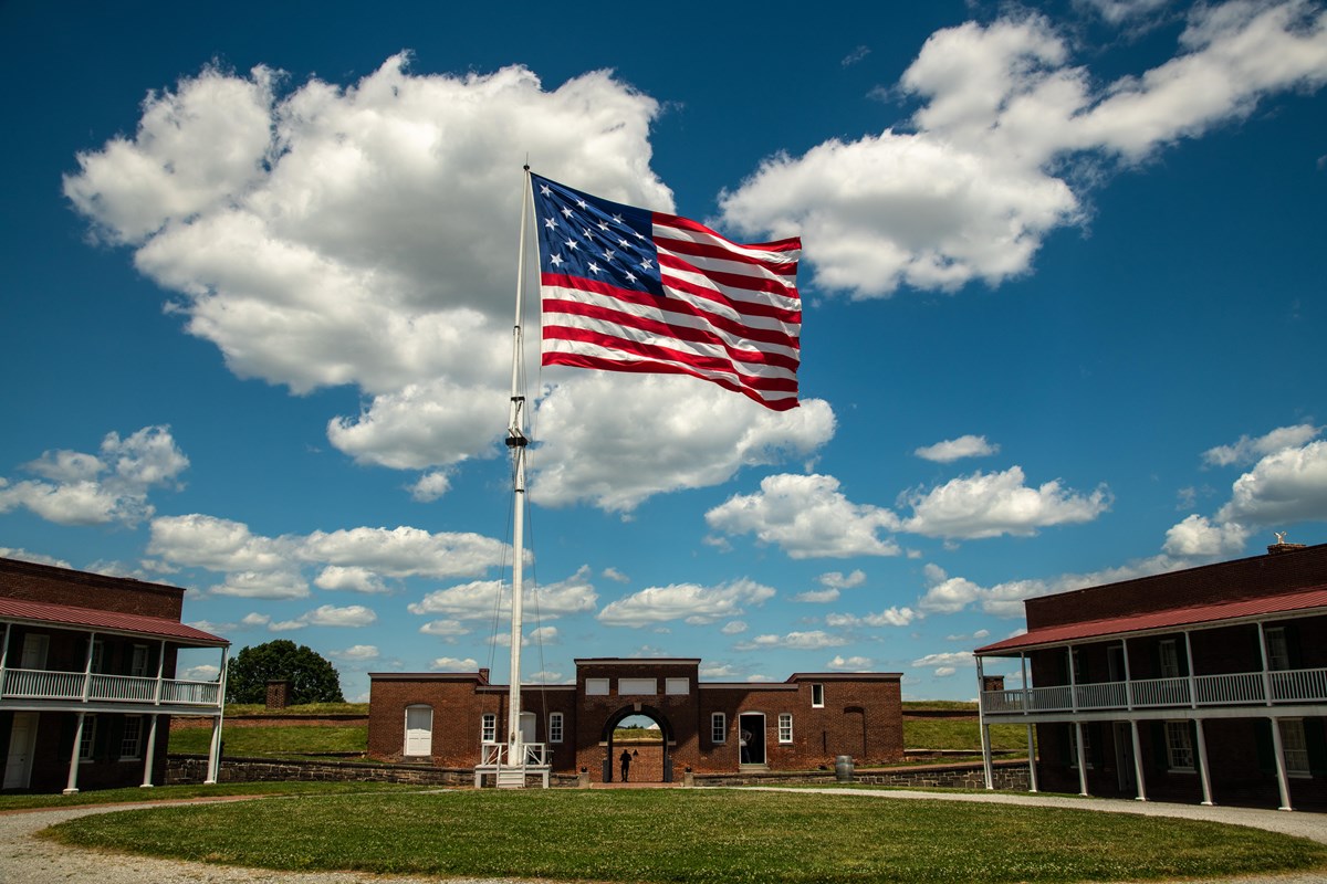 A large American flag waved over the brick sallyport of an old fort. 