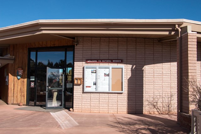 Entrance of the Natural Bridges visitor center with a 'Welcome to Natural Bridges' sign and a bulletin board