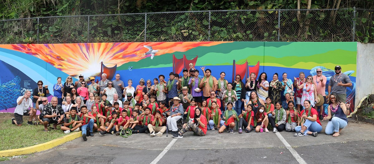 Group of community members pose in front of a large mural