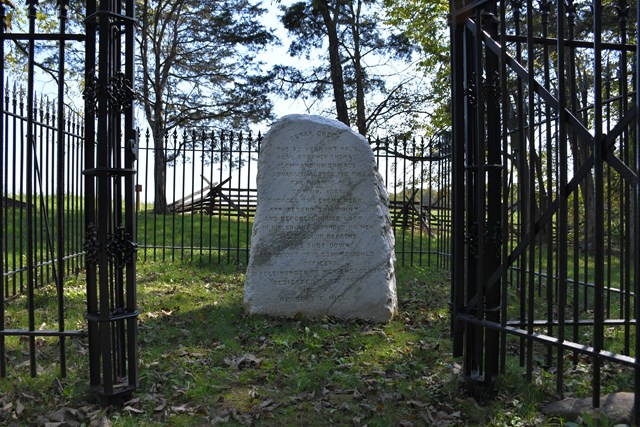 A rough marble monument in an iron-fenced enclosure commemorates Civil War combat.