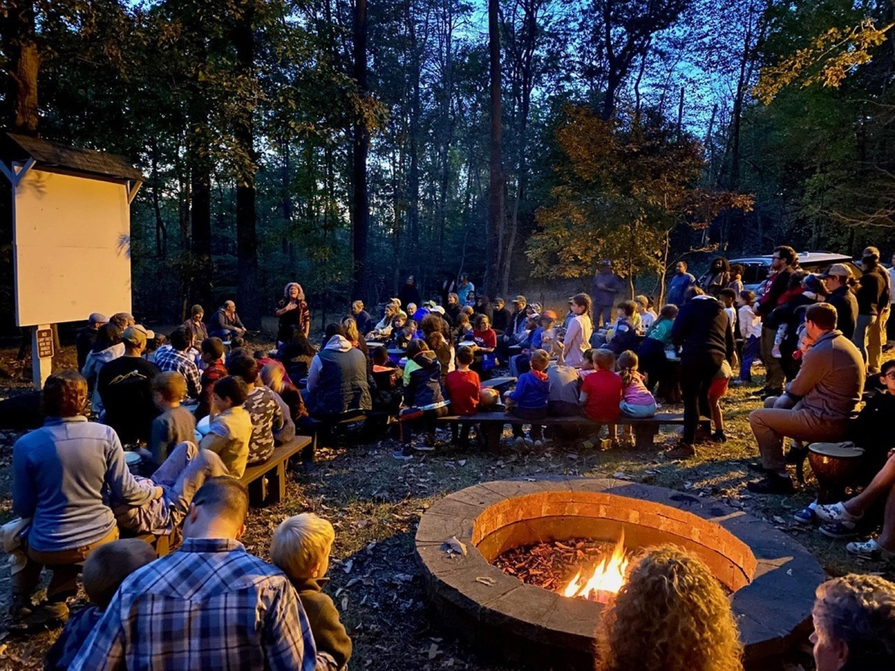 campfire in the forefront and people watching a campfire program in the background